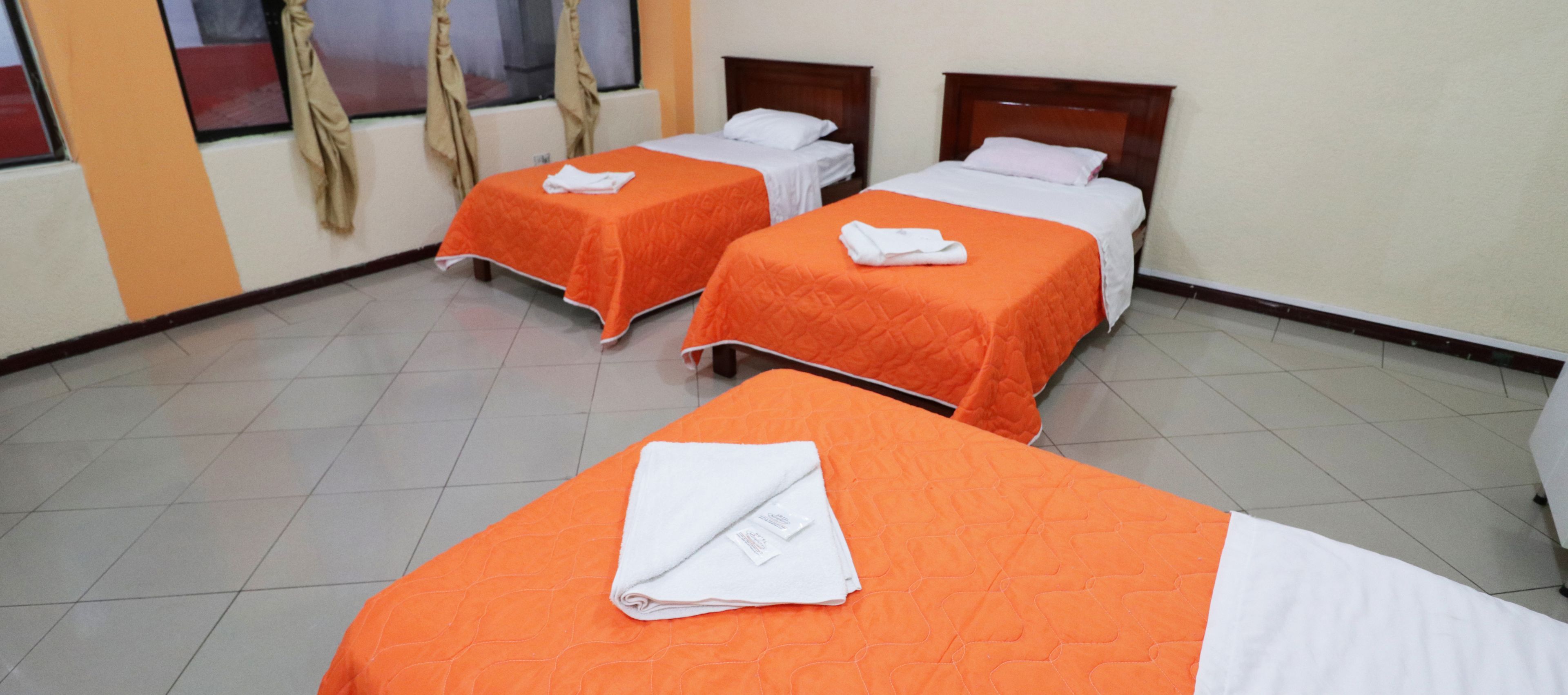Habitación de hotel con dos camas, cada una con cubrecama naranja y almohadas blancas.