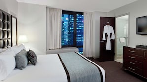 Habitación de hotel con una cama grande, un armario, una televisión y vistas a la ciudad de noche.