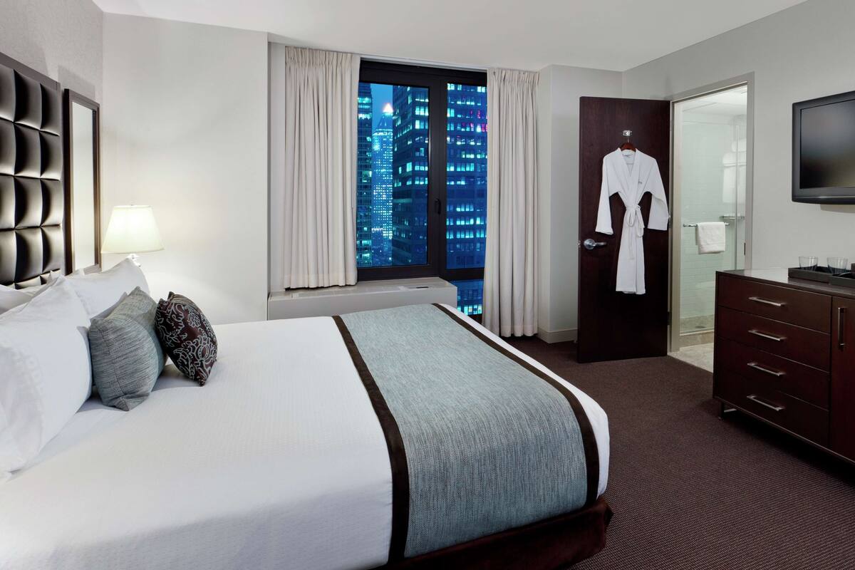 Une chambre d’hôtel avec un grand lit, une armoire, une télévision et une vue sur le paysage urbain la nuit.