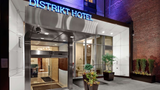 El exterior del Hotel District, con una fachada moderna, entrada de vidrio y plantas en macetas en el área de recepción.