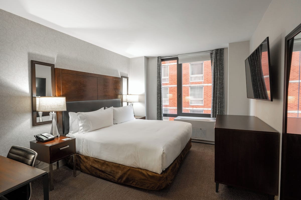 Une chambre d’hôtel avec un grand lit, un bureau, une chaise, une télévision et une fenêtre avec des rideaux.