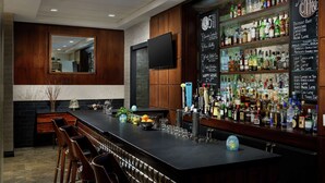 Zona de bar con una barra larga, taburetes, un televisor montado en la pared y un menú en la pared que enumera diversas bebidas.