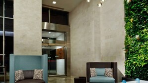 Un vestíbulo con dos sofás, una mesa de centro, luces colgantes, una pared verde y una zona de cocina al fondo.