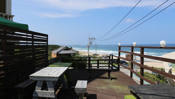A wooden deck with picnic tables overlooking a beach. - Seaview Pension (Gangneung)