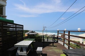 A wooden deck with picnic tables overlooking a beach. - Seaview Pension (Gangneung)