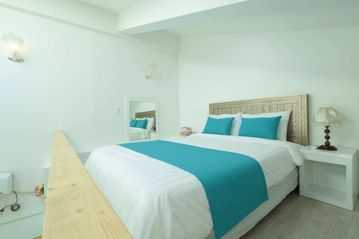 A bedroom with a bed, a nightstand, a lamp, and a mirror.