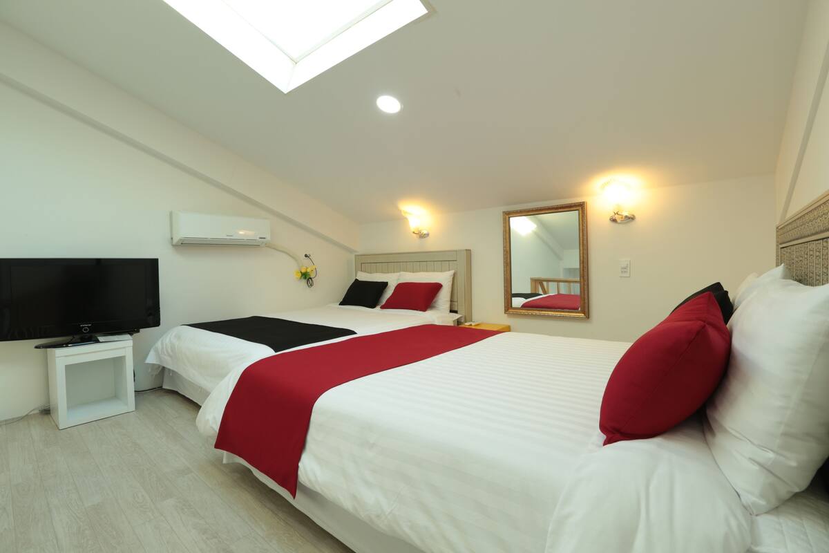 A hotel room with two beds, a flat-screen TV, an air conditioner, and a skylight.