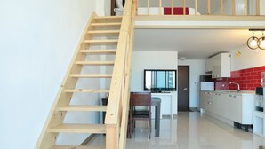 A modern interior with a wooden staircase leading to a loft bedroom, a kitchen with red tiles, and a dining area. - Seaview Pension (Gangneung)