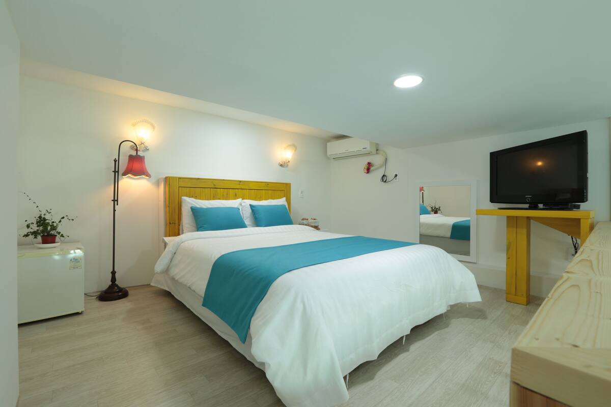 A hotel room with a bed, bedside lamp, air conditioning unit, television, and a desk.