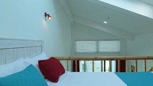 A bedroom with a skylight, a bed with white and teal bedding, and a red pillow. - Seaview Pension (Gangneung)