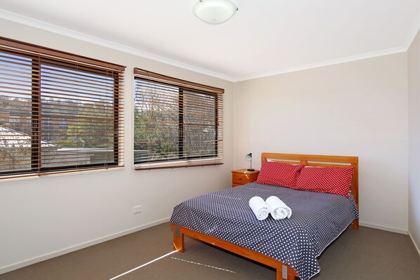 A bedroom with a bed, two windows, a nightstand, and a lamp.