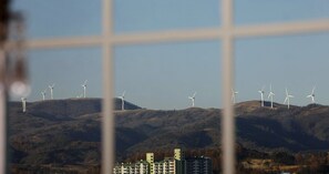 Blick auf Windräder auf einer Hügelkuppe mit Gebäuden im Vordergrund.