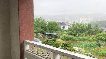 A balcony with a white lattice railing, overlooking a green landscape with trees and buildings.