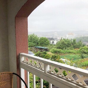 Ein Balkon mit weißem Gittergeländer, der auf eine grüne Landschaft mit Bäumen und Gebäuden blickt.