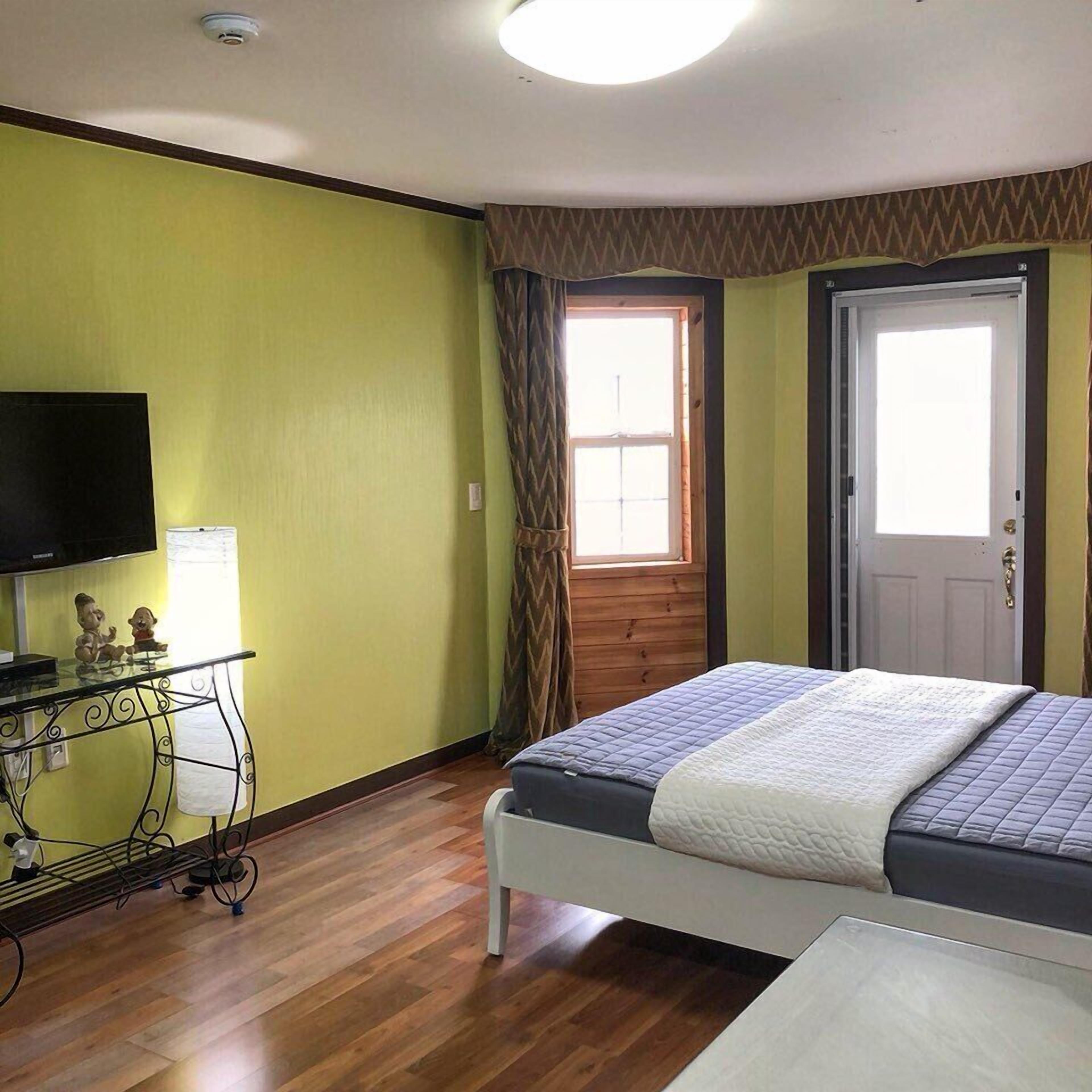 A bedroom with a bed, a television, and a window with curtains.