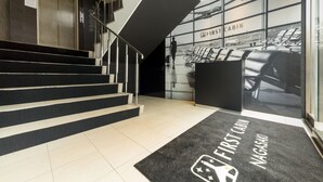 A modern hotel lobby with a staircase leading to an elevator, a reception desk, and a wall displaying airplane images. - First Cabin Nagasaki (Nagasaki)