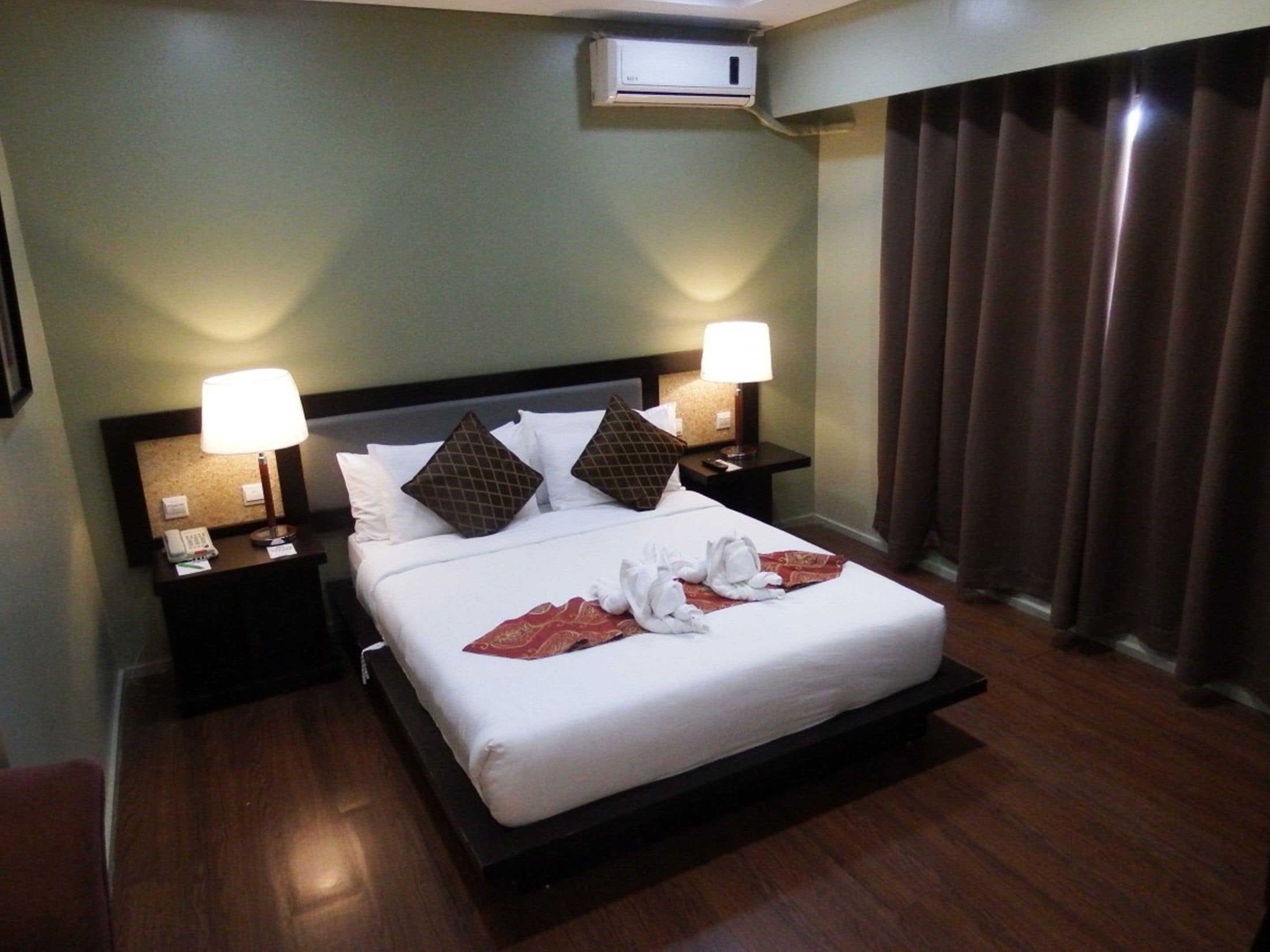 A hotel room with a bed, two bedside lamps, a telephone, and a wall-mounted air conditioner.