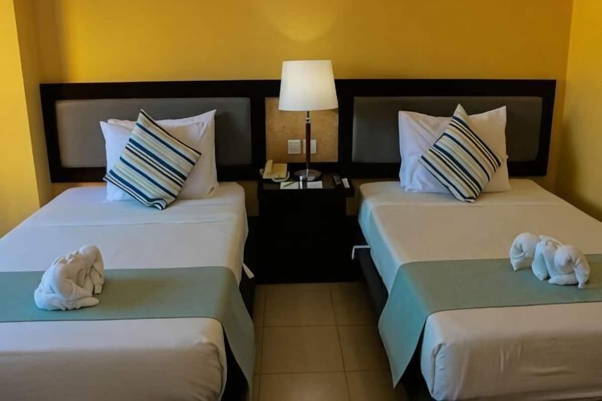 Two twin beds with pillows, a nightstand with a lamp, and a towel on each bed.