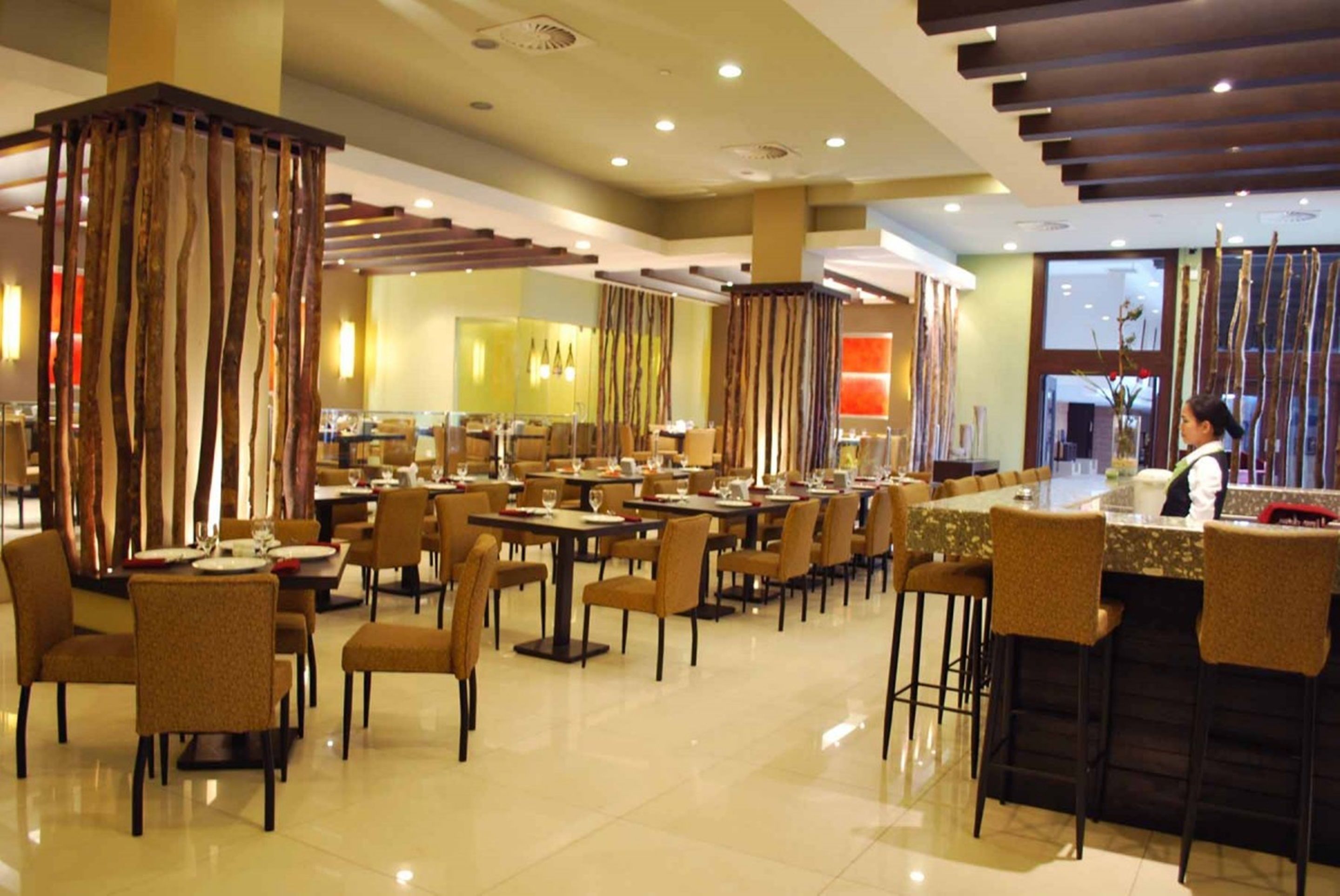A spacious restaurant with multiple dining tables and chairs, a bar area, and decorative wooden panels.