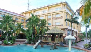 A hotel with a swimming pool, palm trees, and a thatched-roof gazebo. - Tanza Oasis Hotel and Resort (Tanza)