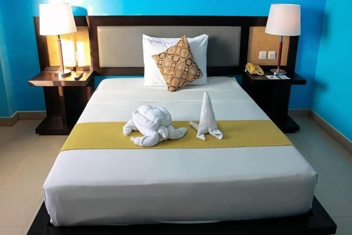 A hotel room with a bed, two bedside lamps, a telephone, and a pillow with a circular pattern.