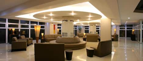 A spacious lobby with a central circular seating area, large windows, and a modern ceiling design.