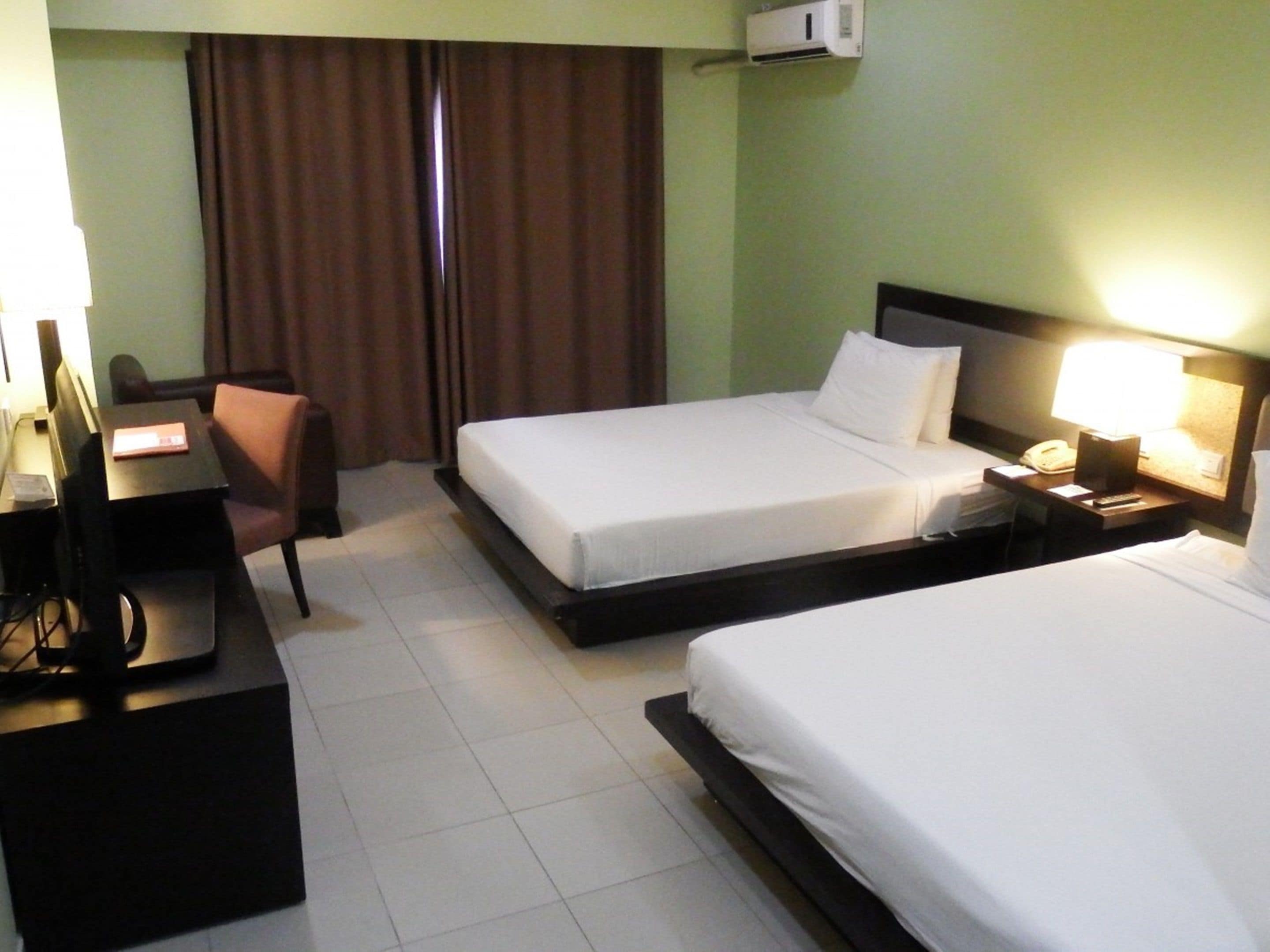 Een hotelkamer met twee bedden, een bureau, een stoel, een nachtkastje en een airconditioning.