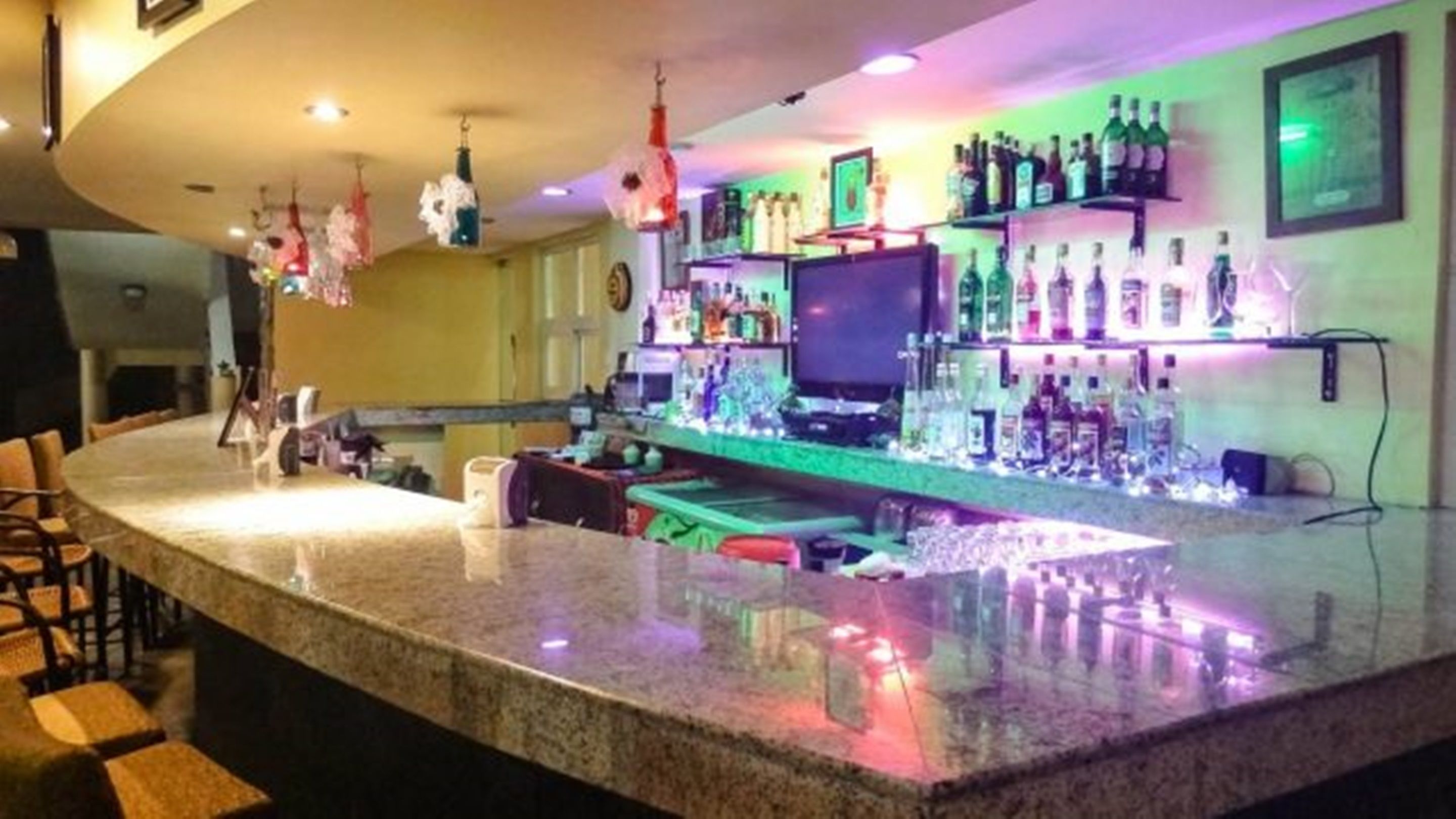 Een bar met een granieten aanrecht, barstoelen en diverse flessen drank.