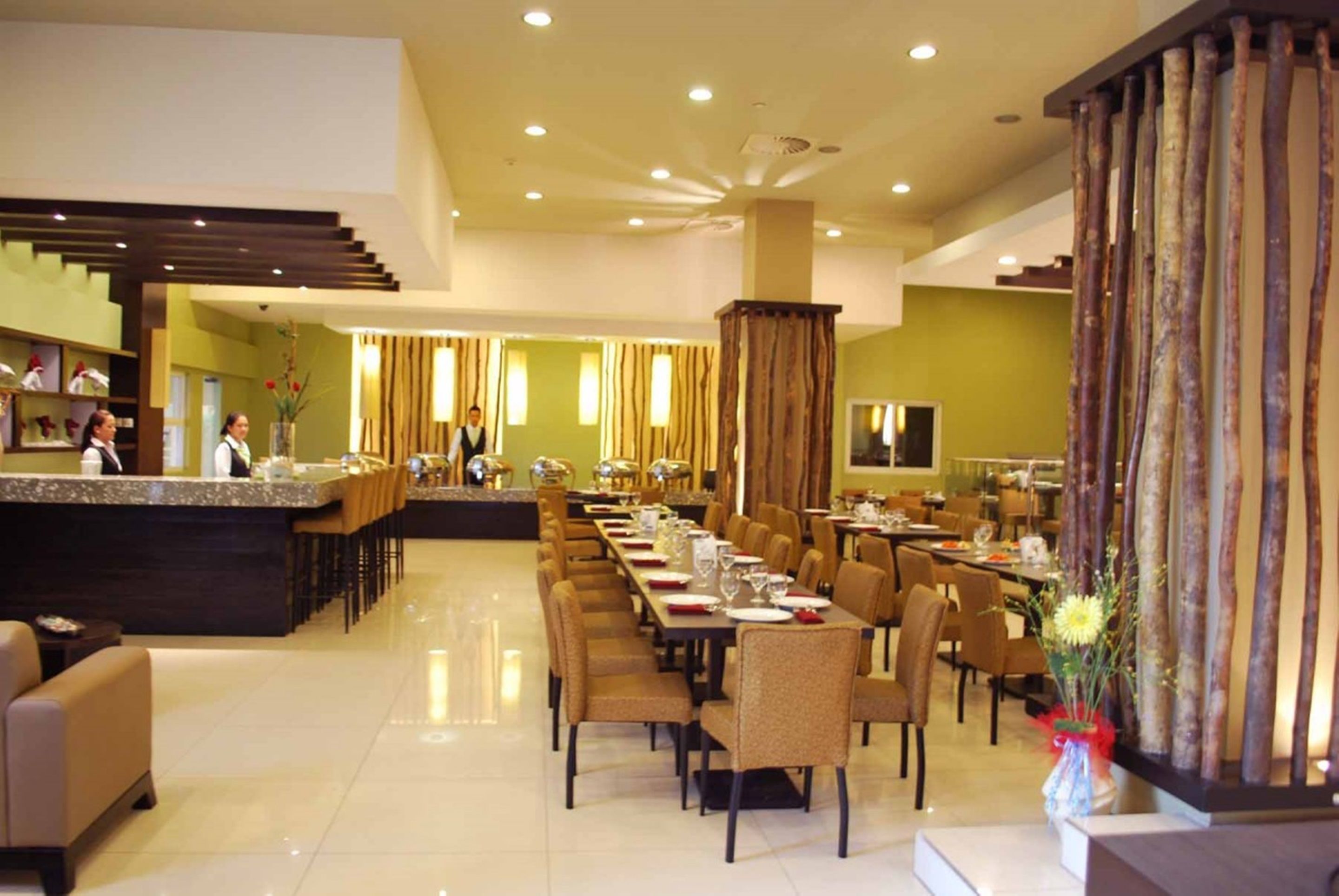 Un comedor de hotel con una larga mesa común, mesas individuales y una zona de bar.