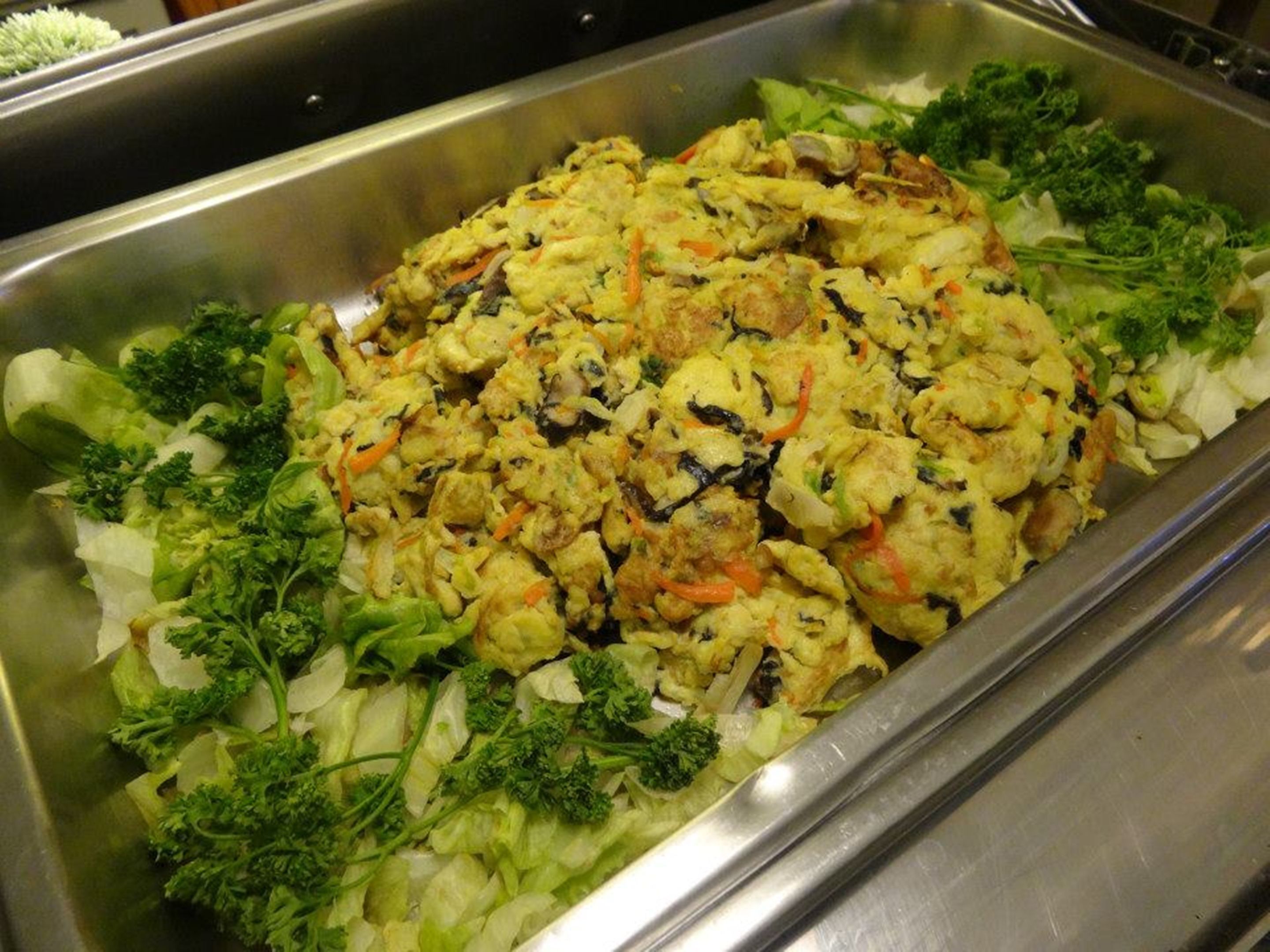 A buffet with a variety of dishes, including a large salad with mixed greens and vegetables.