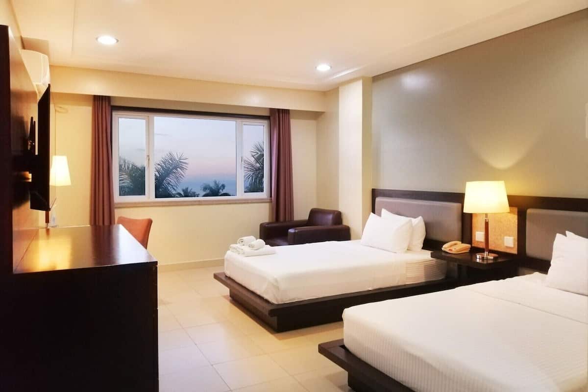 A hotel room with a bed, a desk, a chair, a nightstand, and a window with a view.