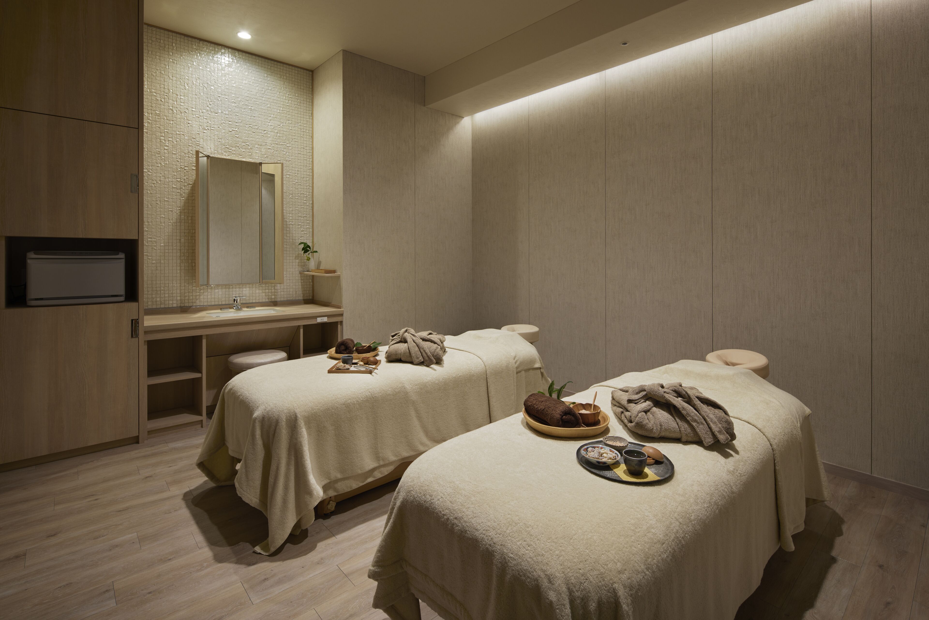 A spa room with two treatment beds, a sink, and a mirror.