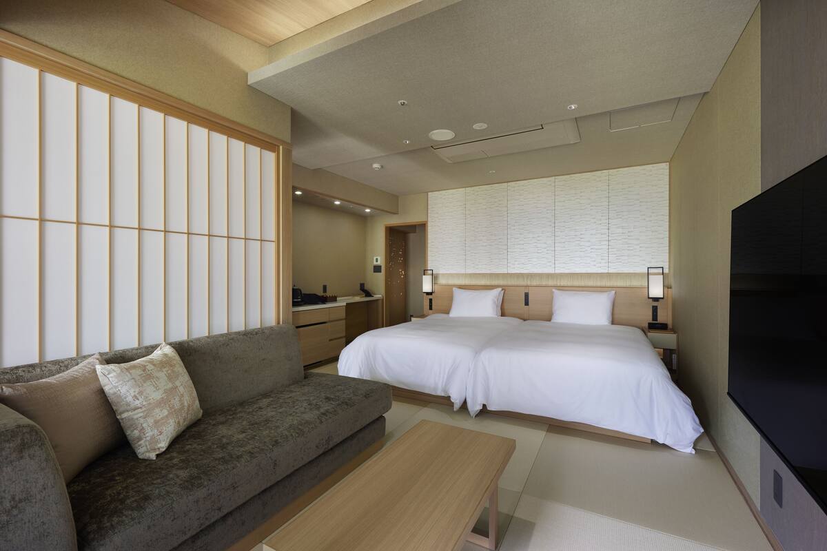 A hotel room with a large bed, a sofa, a desk, and a TV.