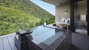 A modern outdoor hot tub with a glass enclosure, overlooking a lush green hillside. - Hatsuhana (Hakone)