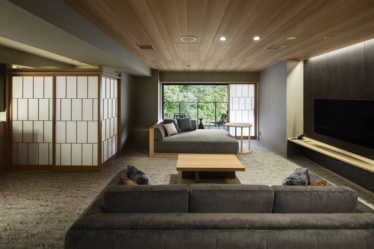 A modern living room with a sofa, a coffee table, and a television. There is a sliding door with a view of greenery outside.