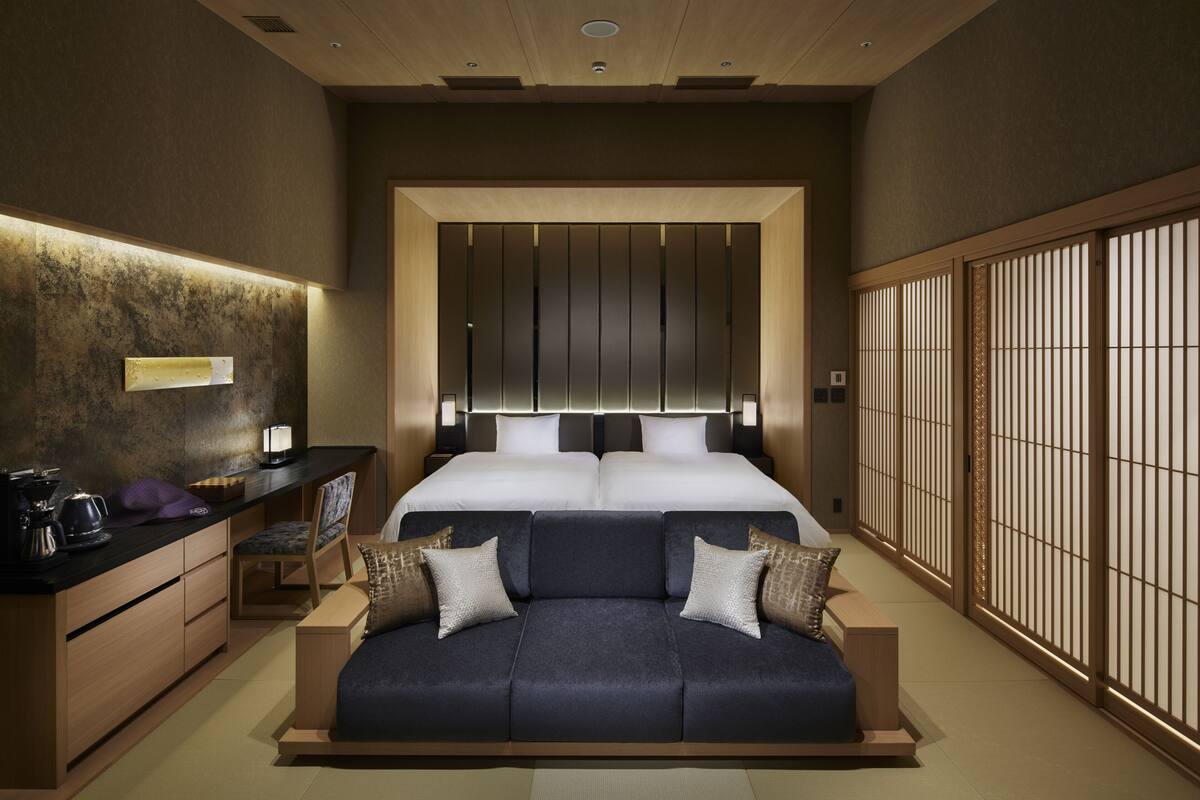 A modern bedroom with a large bed, a sofa, a desk, and a traditional sliding door.