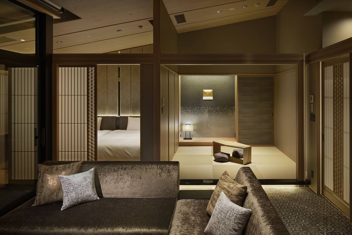 A modern hotel room with a sofa set, a bed, and a small desk area.