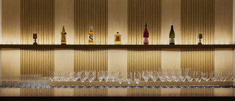 A bar area with a row of wine glasses and bottles of liquor on a shelf against a wall with vertical lines.