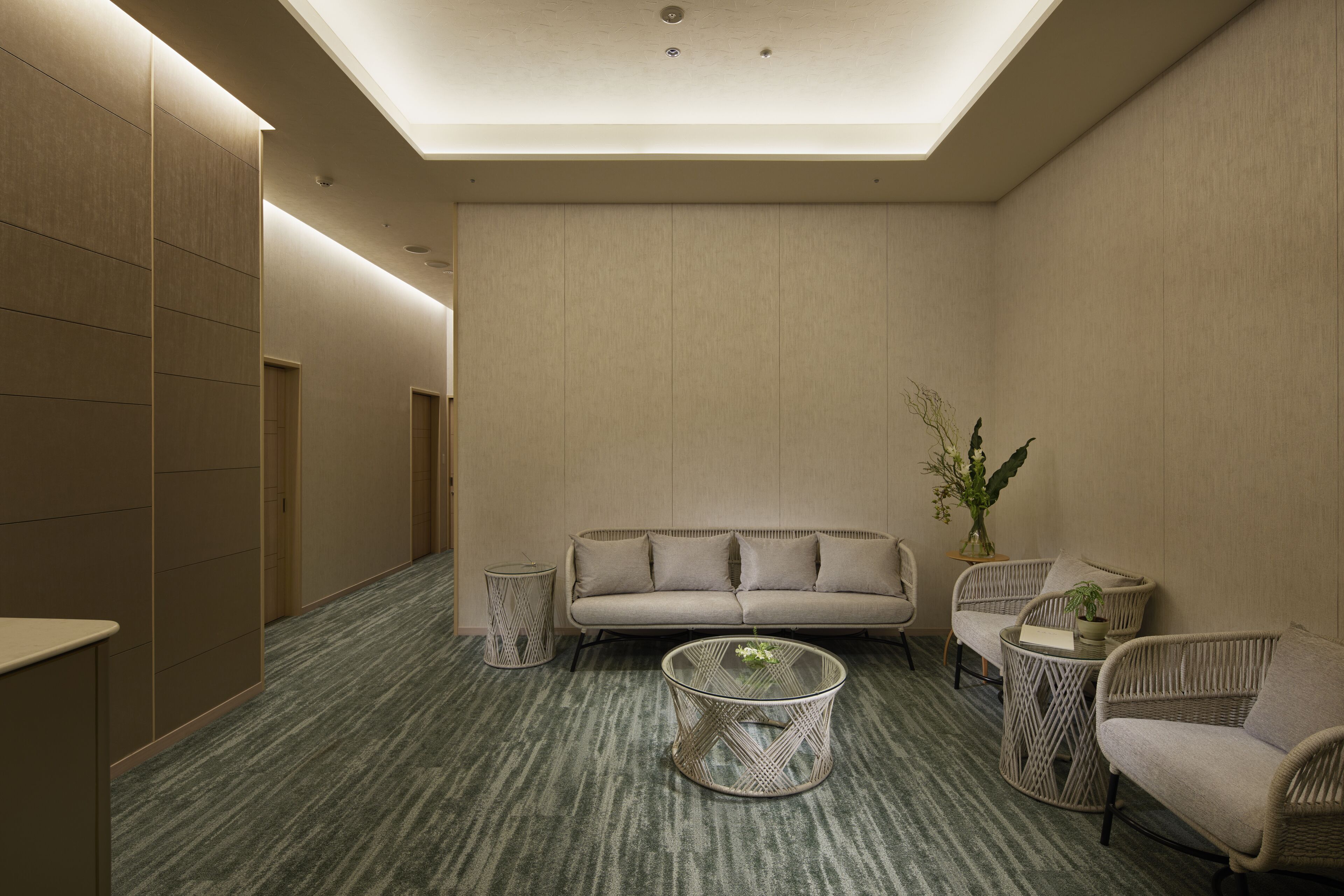 A modern, well-lit lounge area with a sofa, two wicker chairs, a round coffee table, and a small side table with a plant.