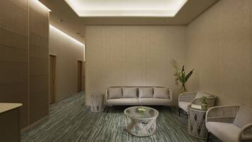 A modern, well-lit lounge area with a sofa, two wicker chairs, a round coffee table, and a small side table with a plant.