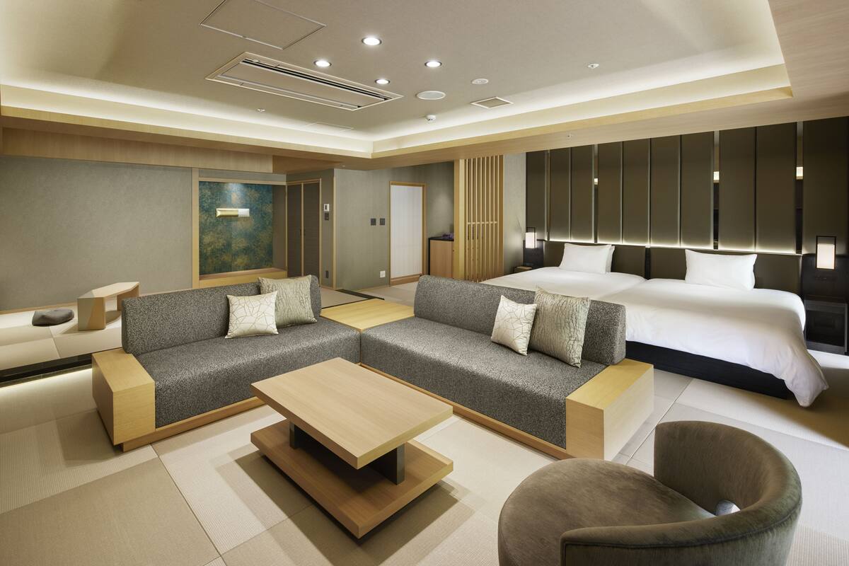 A modern hotel room with a large bed, two sofas, a coffee table, and a seating area.