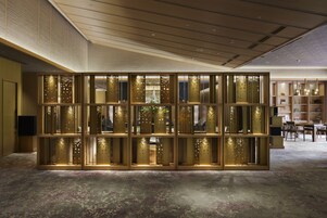 Un interior moderno con un separador decorativo que presenta intrincados diseños calados, piso de concreto pulido y una habitación bien iluminada con techo enrejado e iluminación empotrada.