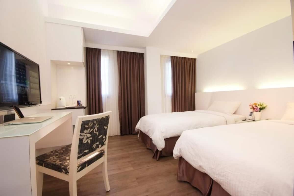 A hotel room with a desk, two beds, a TV, and curtains.