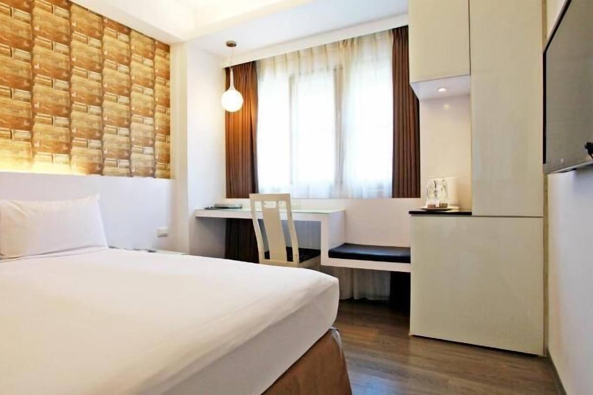 A hotel room with a bed, a desk, a chair, a TV, and a refrigerator.