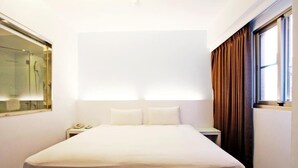A hotel room with a large bed, a bedside table with a lamp, a mirror, and a window with curtains. - Yes Hotel (Taitung)
