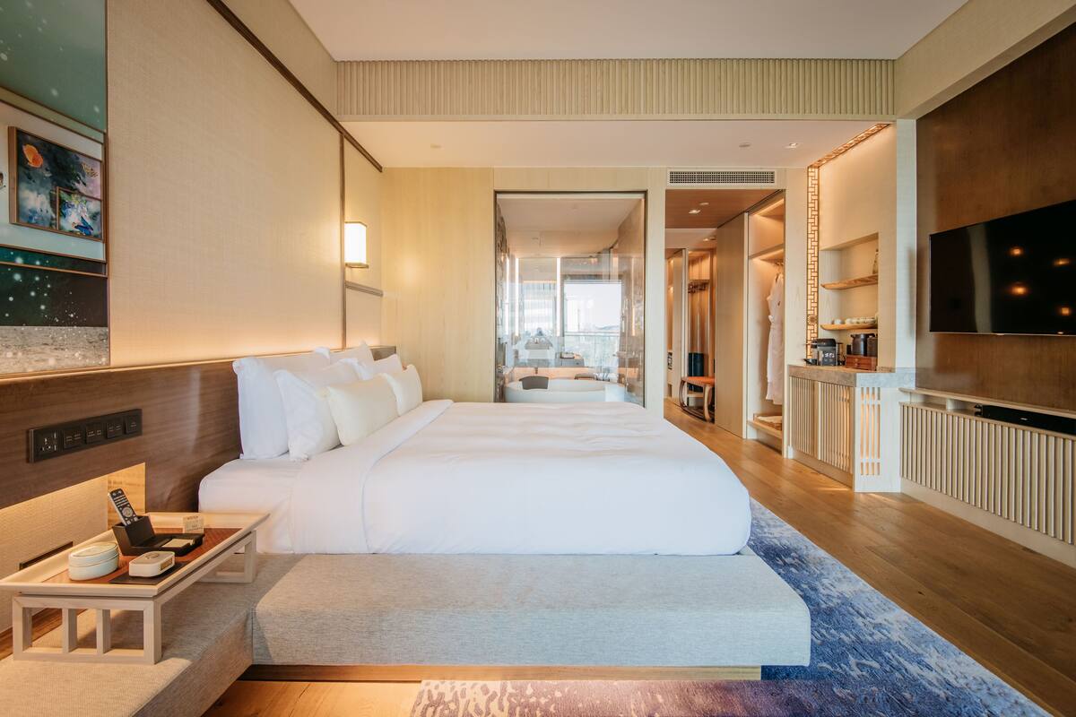 A modern hotel room with a large bed, bedside table, and a TV.