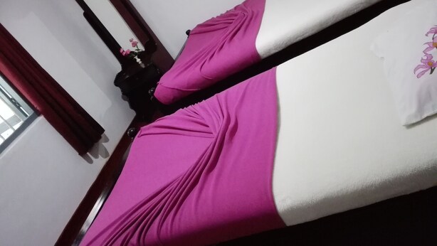 A bed with a white and pink bedspread, a wooden headboard, and a mirror on the wall. - Kumara Sevana - The Family Cottage (Seetha Eliya)