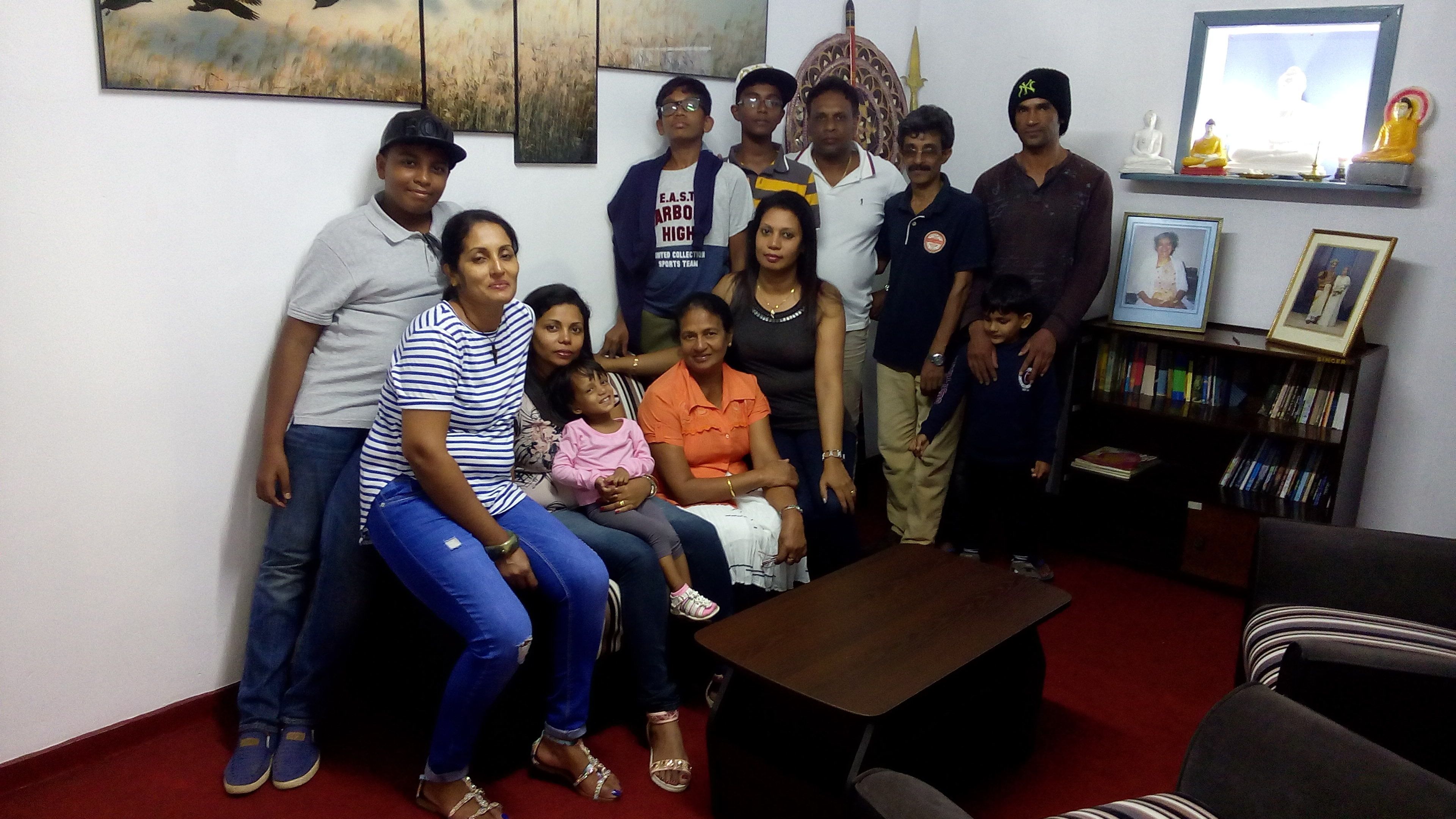 A group of people in a room with a bookshelf, a Buddha statue, and a framed picture on the wall.