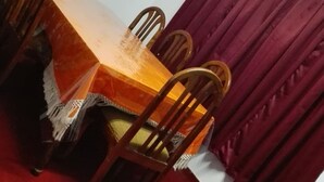 A dining area with a wooden table and chairs, a red carpet, and a window with a curtain. - Kumara Sevana - The Family Cottage (Seetha Eliya)