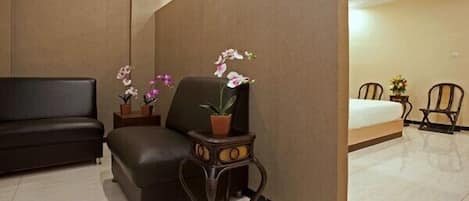 A hotel room with a dark leather sofa, a small wooden side table with a potted orchid, a large window, and a bed with a white mattress.